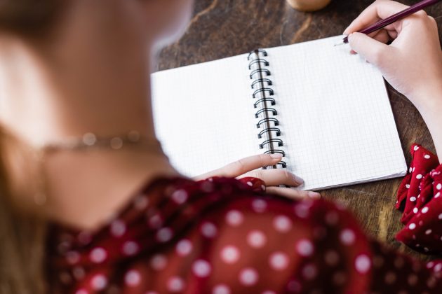 selective focus of student writing in notebook with pencil in apartment